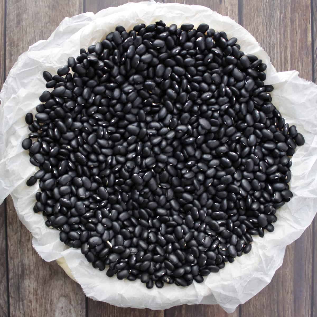 unbaked pie shell lined with black beans on parchment paper