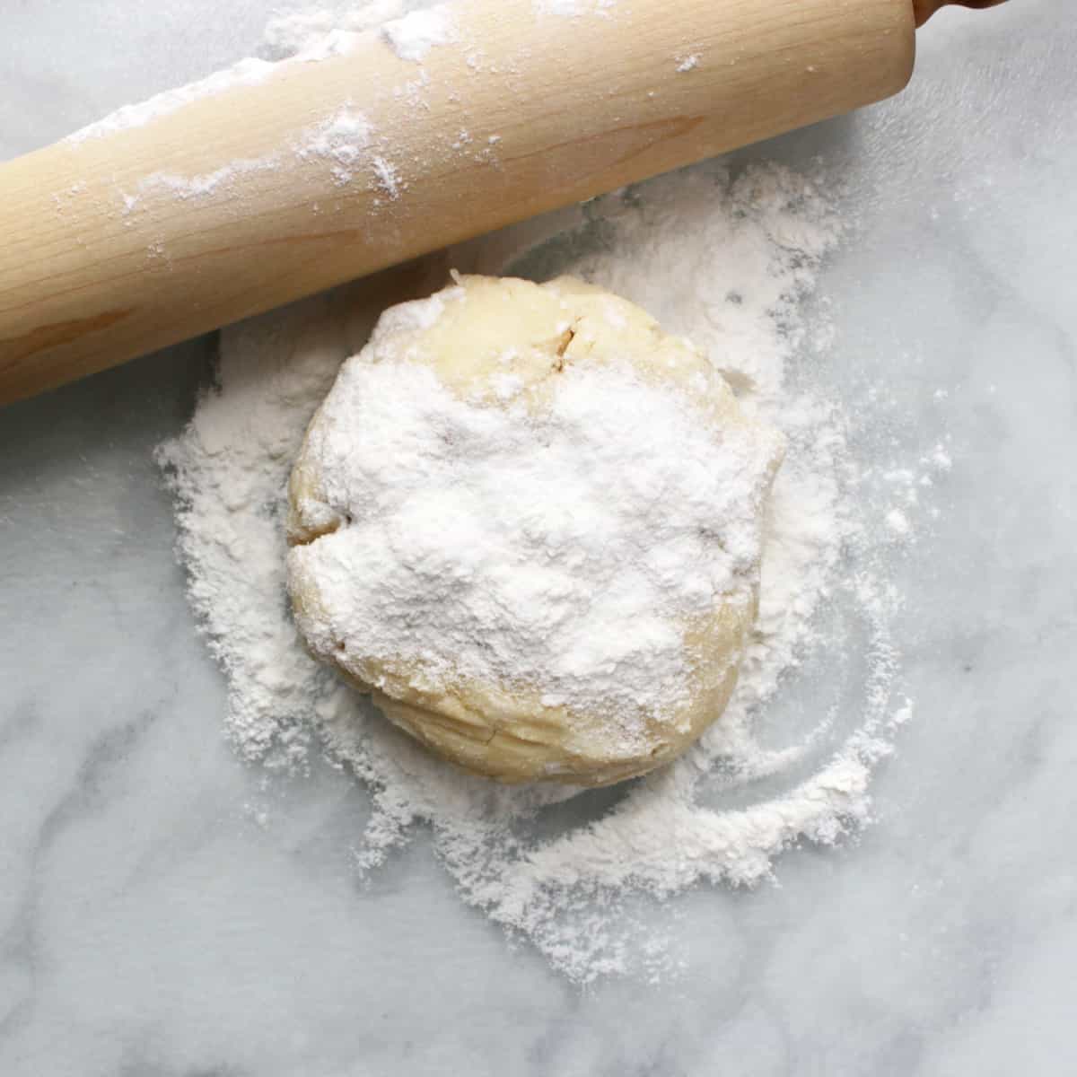 floured ball of pie dough on marble with wooden rolling pin