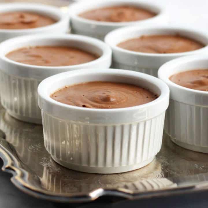 several white ramekins filled with chocolate pudding sit on a silver tray