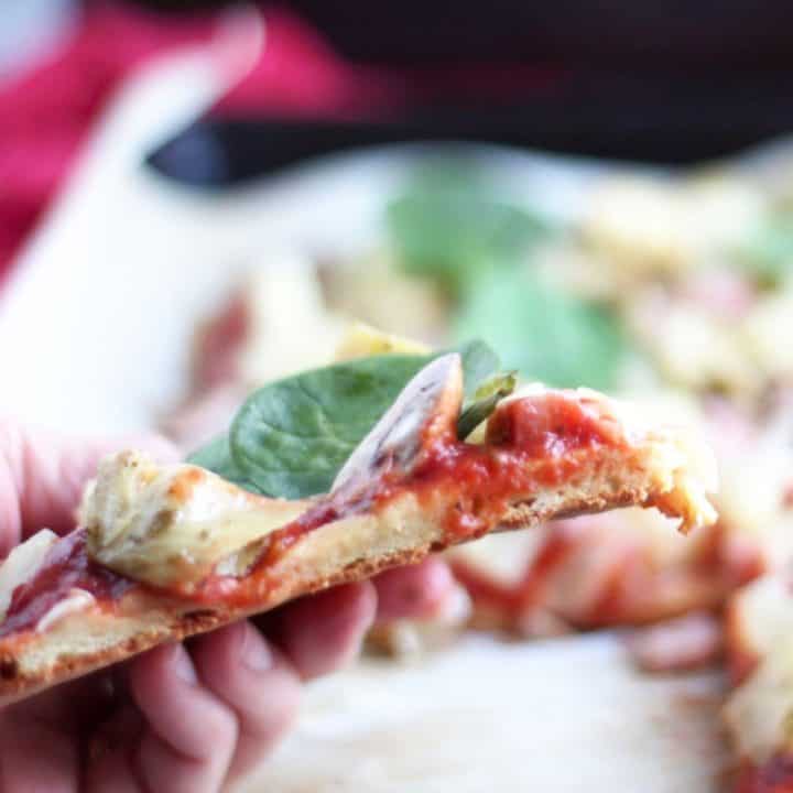 slice of thin-crust pizza held in hand