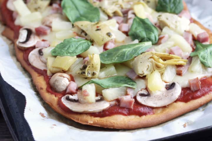 gluten free pizza crust with tomato sauace, mushrooms, pineapple, and basil