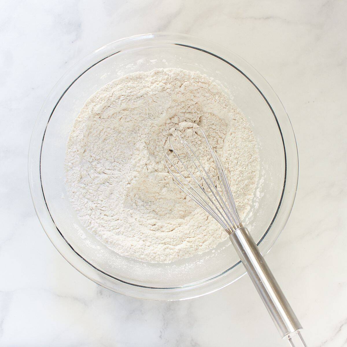 white, gluten-free flour ingredients whisked together in a clear glass bowl.