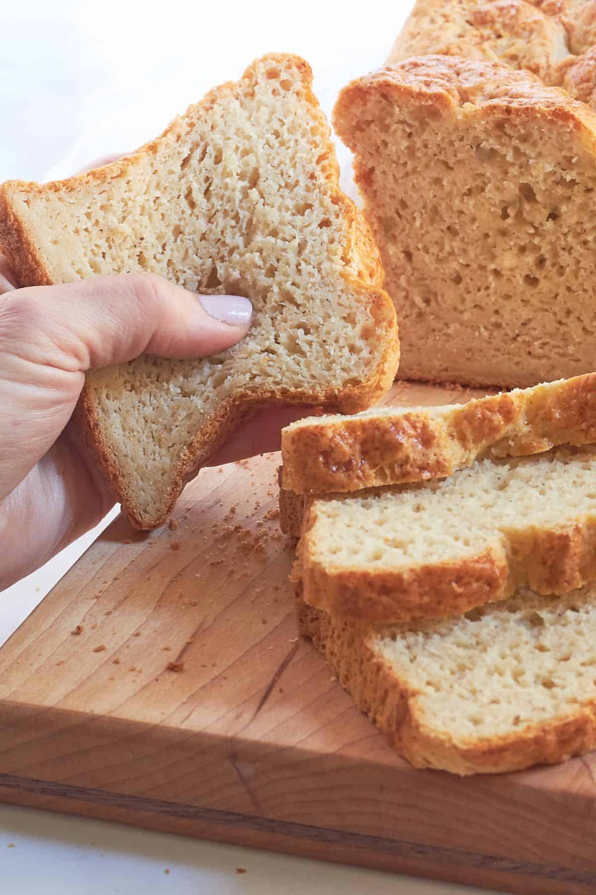 a hand holds a slice of gluten-free brioche bread, showing how soft it is.