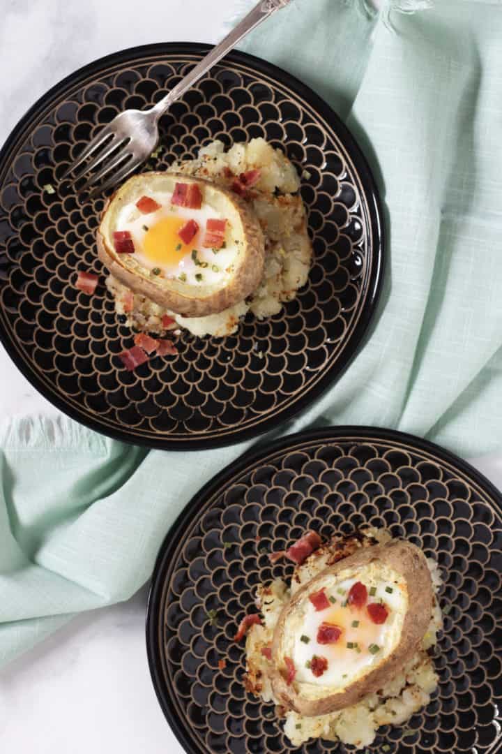 flat lay of egg-stuffed baked potatoes garnished with bacon and chives on black plates