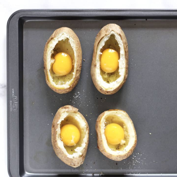 raw egg in each of four scooped out baked potato shells on tray