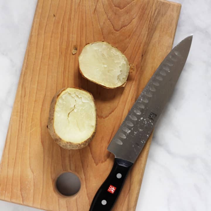 overhead view of baked potato with top sliced off on wooden cutting board with chef's knife