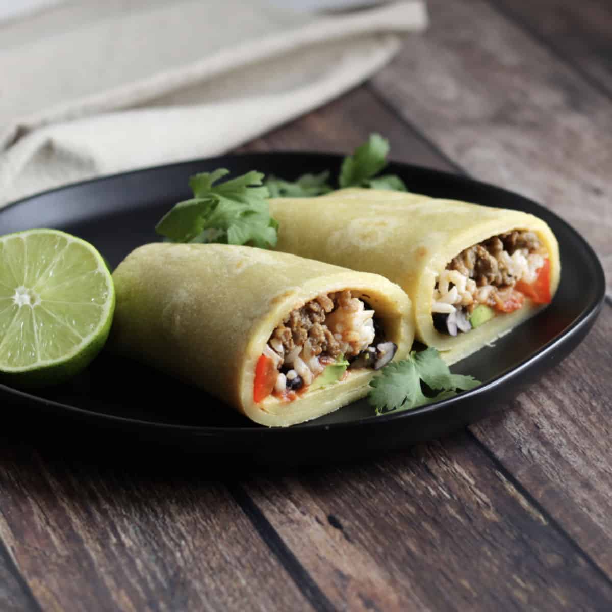 two homemade burritos cut with open ends exposed, with lime and cilantro on black plate
