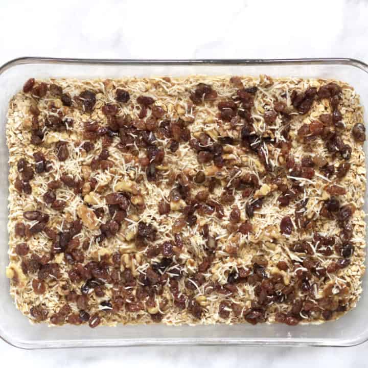 raisins, coconut, and nuts spread over oat layer in glass pan