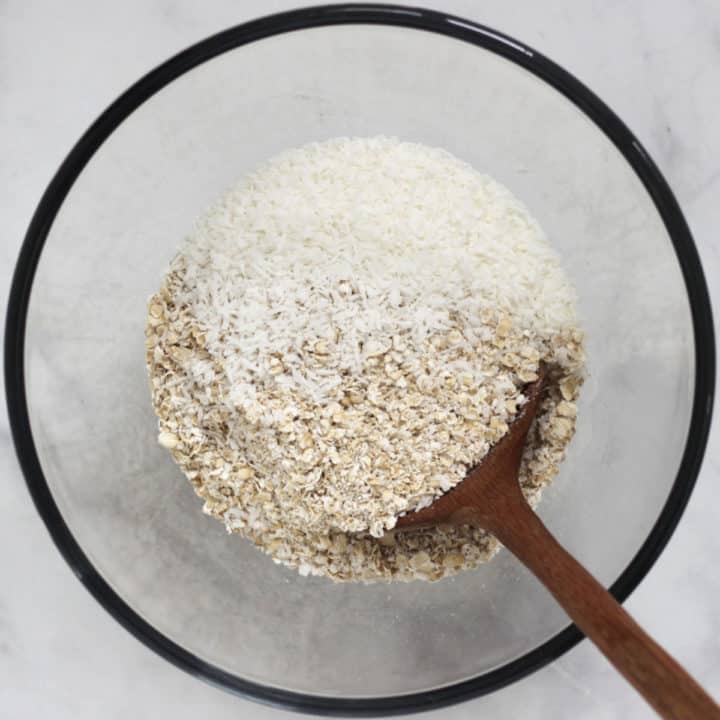 dry oats and coconut stirred in a glass bowl with a wooden spoon