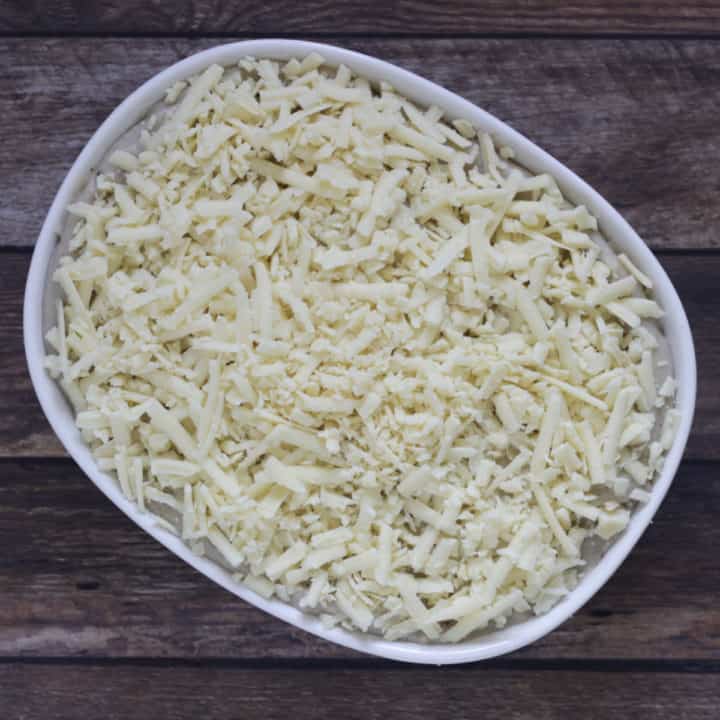 shredded white cheese over scalloped potatoes in baking dish