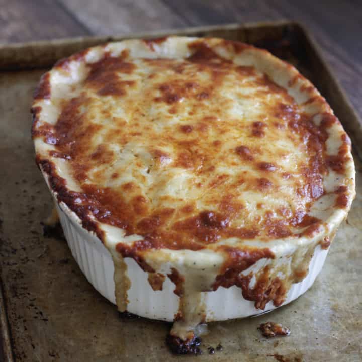 baked scalloped potatoes with golden browned cheese dripping over the sides onto an old baking sheet