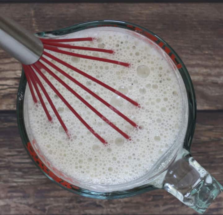 red whisk in foamy white liquid in saucepan