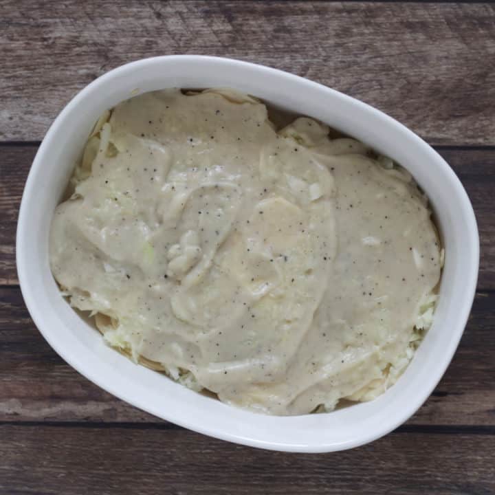 layer of white cream sauce spread over a layer of slices potatoes in baking dish
