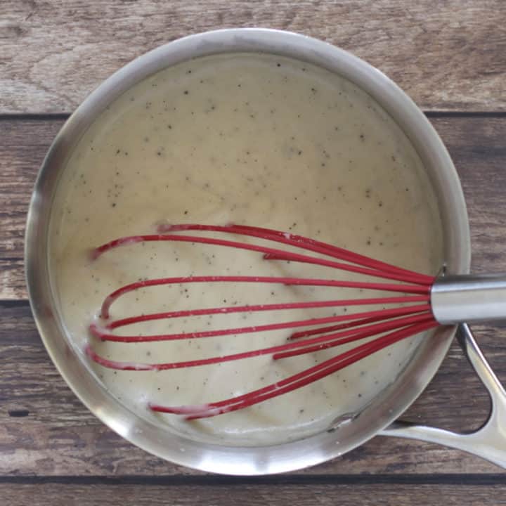 red whisk in foamy white liquid in saucepan