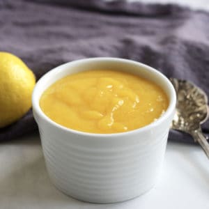 lemon curd in white ramekin with purple linen and a whole lemon in background