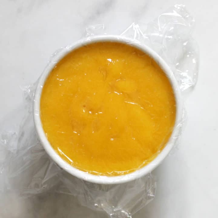 clear plastic pressed against the surface of cooked lemon curd in white bowl