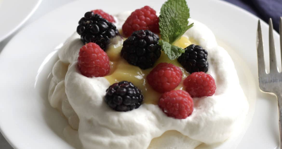 raspberries and blackberries nestled into whipped cream on a meringue base