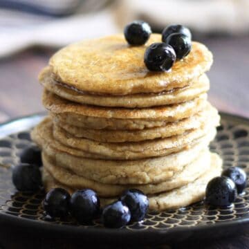 stack of golden pancakes, topped with syrup and blueberries.