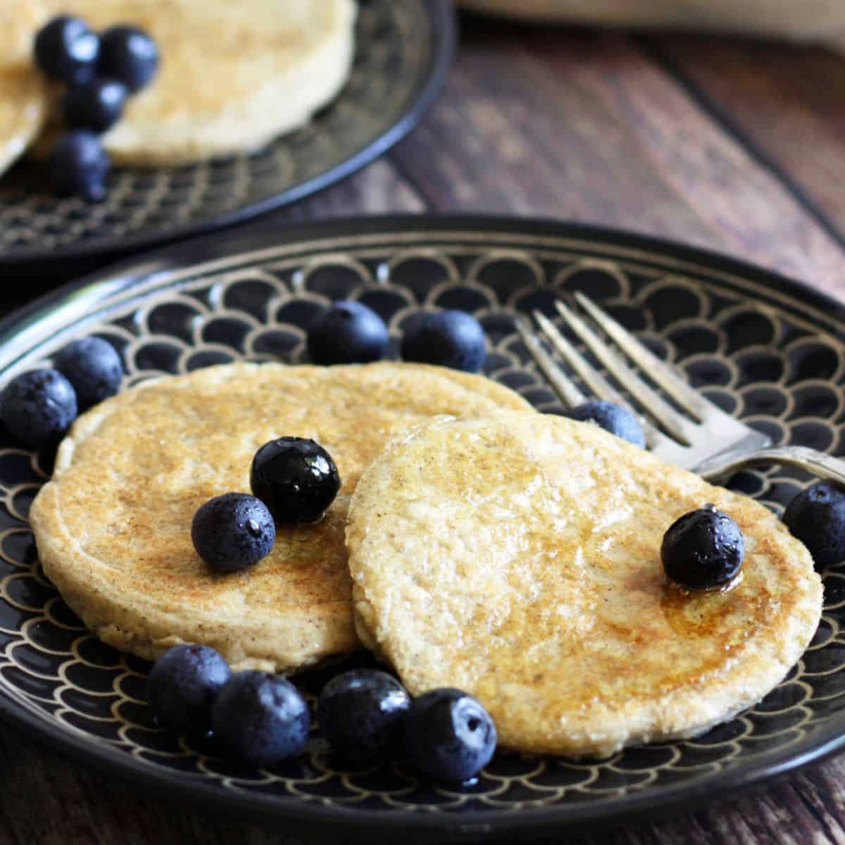 two pancakes on a black plate, topped with blueberries