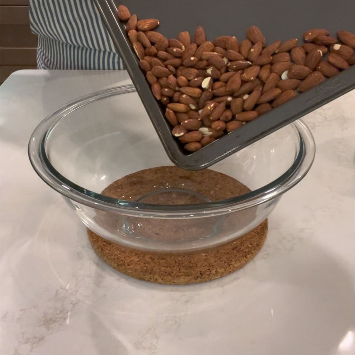toasted almonds being poured from baking sheet to pyrex bowl.