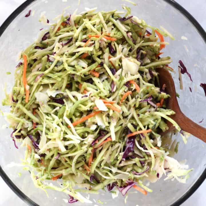 shredded cabbage and broccoli being stirred with wooden spoon in glass bowl