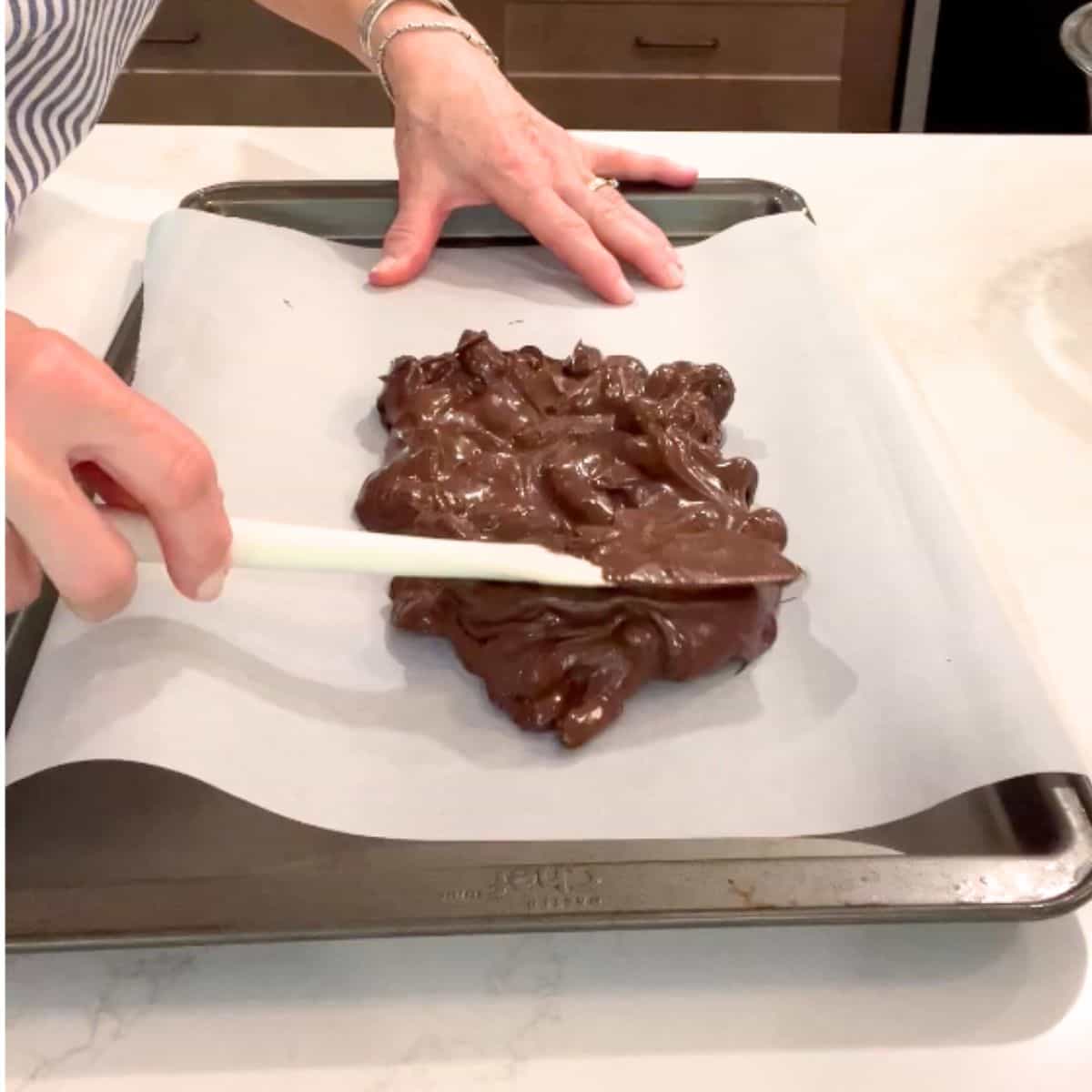 chocolate coated almond mixture is spread out onto a parchment-lined baking sheet.