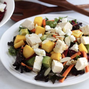cubes of chicken, mango, and avocado sit with slivers of carrot and beet on lettuce and kale salad