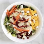 looking down on a round bowl with slivered carrots and beet, on cubed chicken, mango, avocado, and lettude