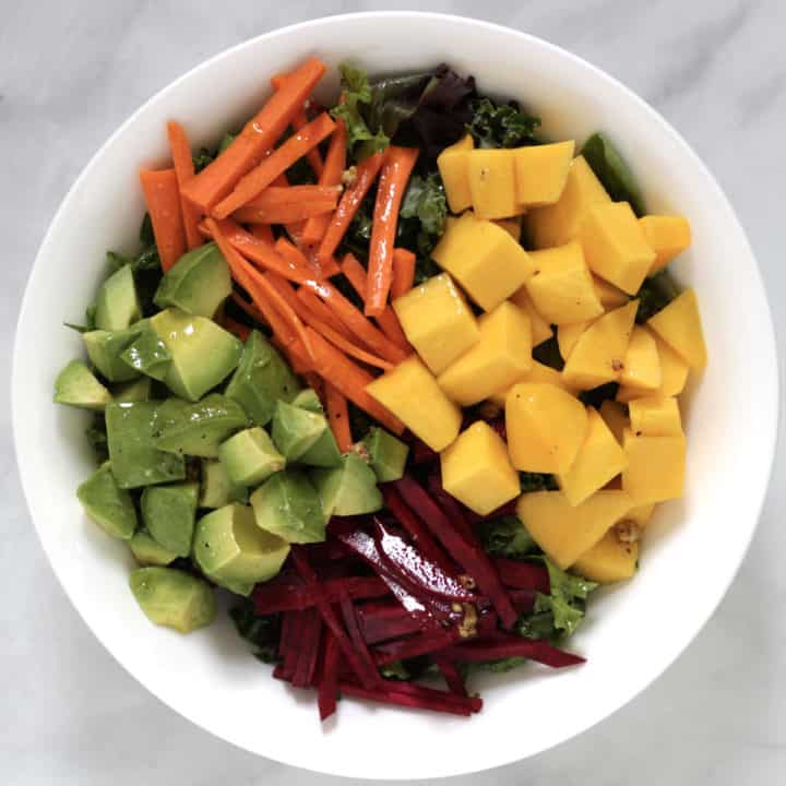 cubes of mango and avocado arranged in white bowl with slivers of beet and carrot, all glistening with salad dressing