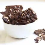 broken pieces of chocolate bark with almonds in it jutting up from a white bowl.