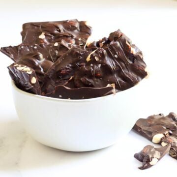 broken pieces of chocolate bark with almonds in it jutting up from a white bowl.