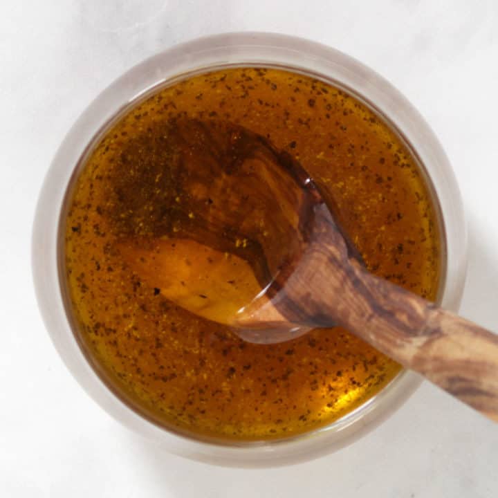 clear, golden salad dressing in glass bowl with wooden spoon