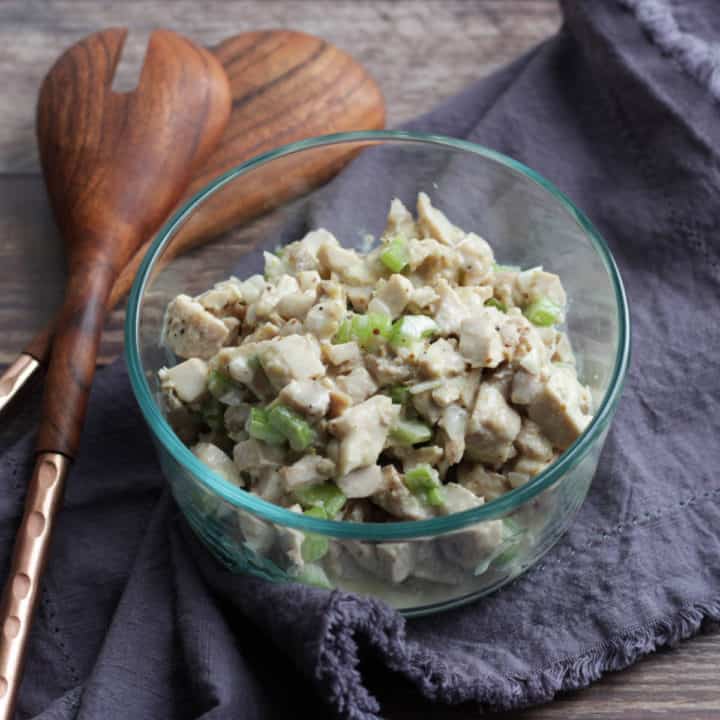 clear bowl of chopped chicken and celery with dressing on lavender napkin with wooden spoons