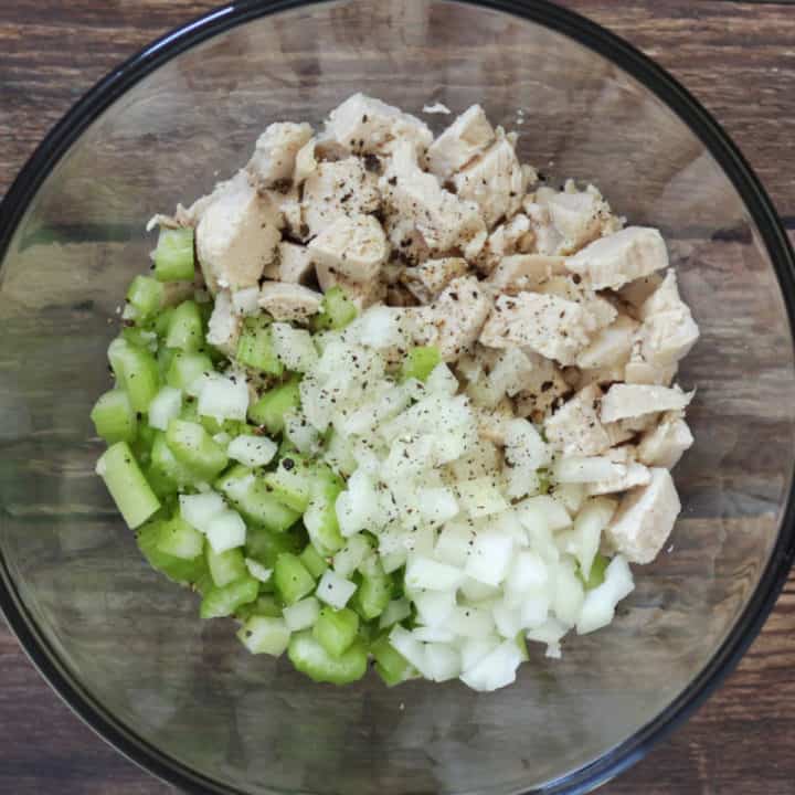 chunks of chicken, chopped celery, and onion sitting in separate sections in bottom of glass bowl