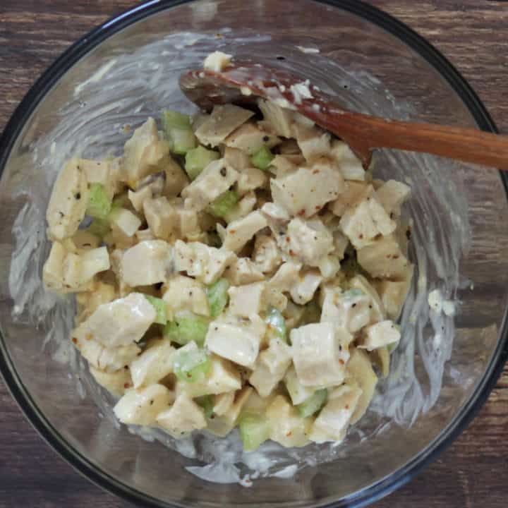 chicken salad stirred with wooden spoon in glass bowl