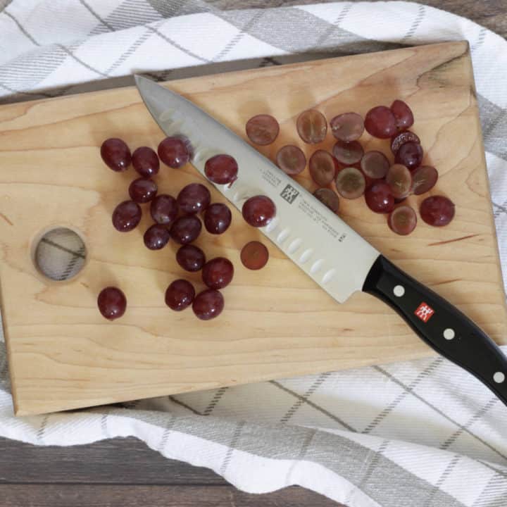 knife with whole and half grapes on wooden cutting board