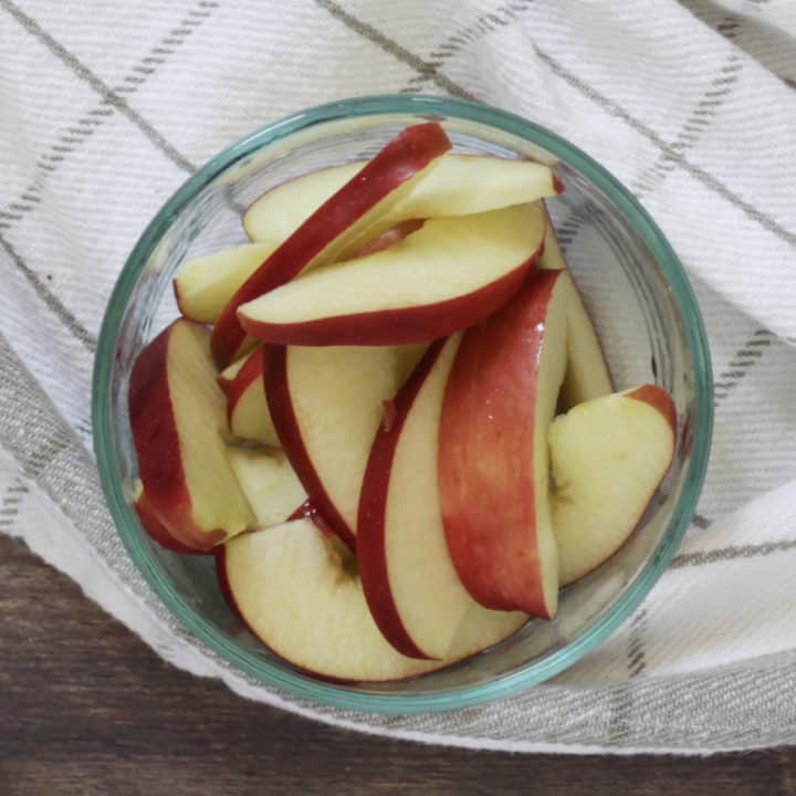 apple slices in glass bowl sitting on white, checked towel