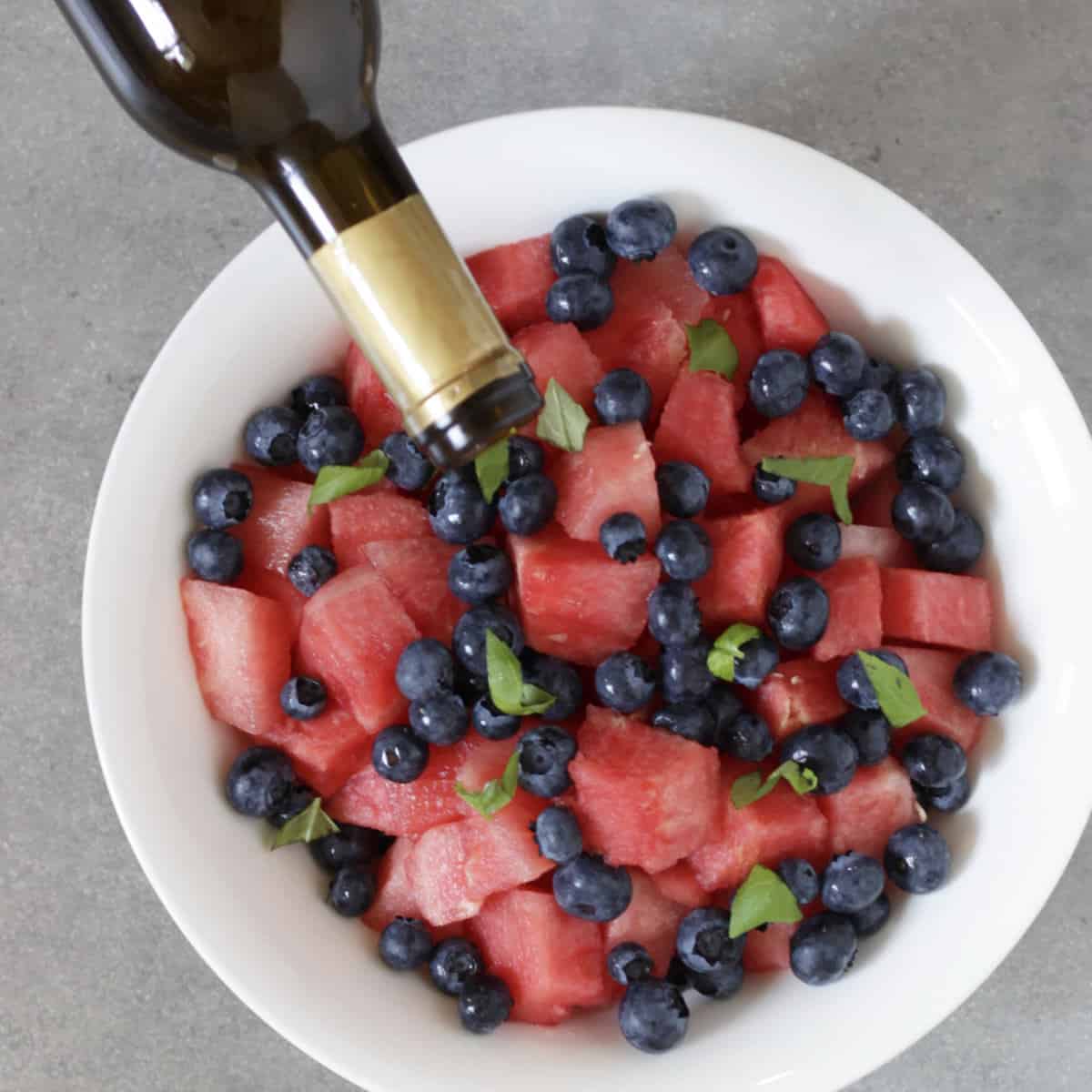 balsamic vinegar being drizzled from bottle over watermelon salad