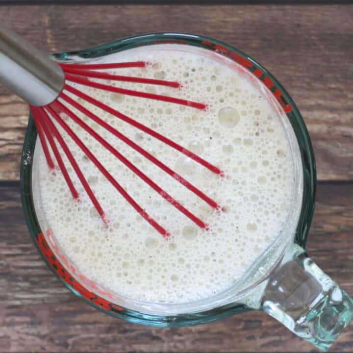 red whisk in foamy milk in measuring cup.