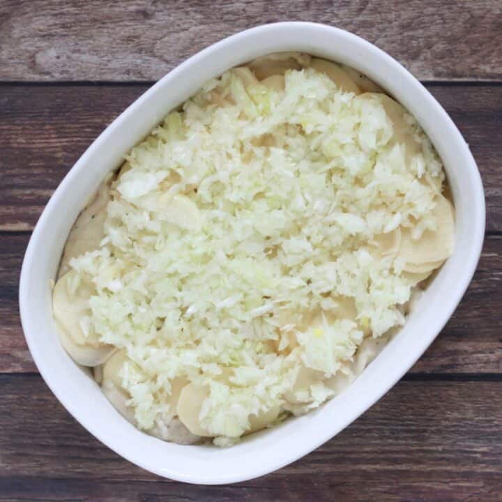 chopped onions over sliced potatoes and cream sauce in casserole dish.