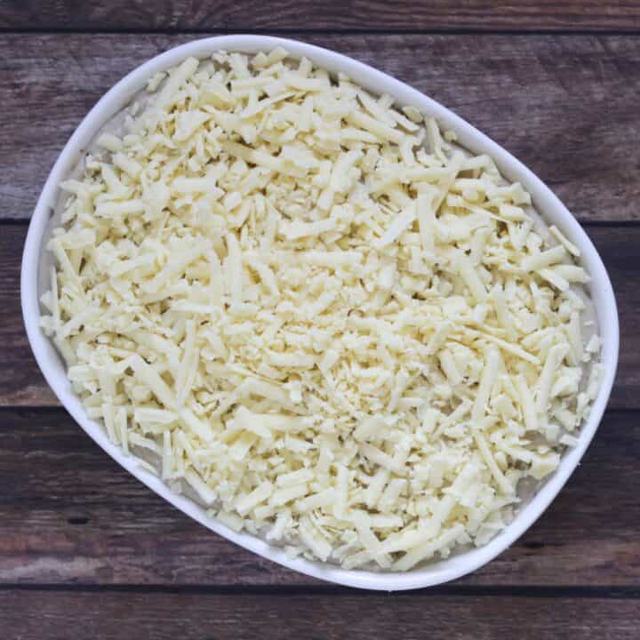 shredded cheese over unbaked scalloped potatoes in white casserole dish.