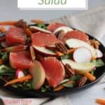 closeup of grapefruit salad on black plate with slim carrot sticks in foreground