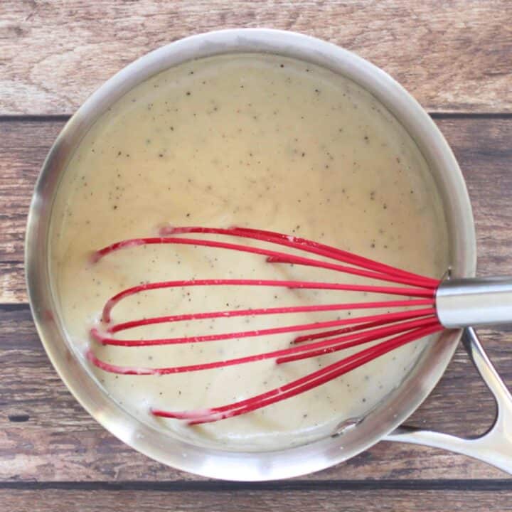 red whisk in thickened white sauce in saucepan.
