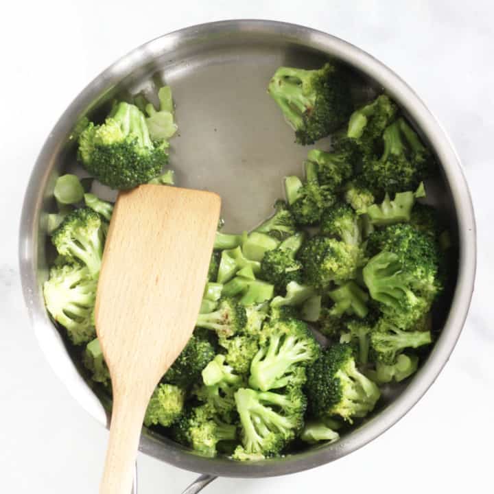 wooden spatula pulling away some broccoli in pan to reveal little liquid