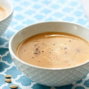 closeup angle of creamy golden soup in white bowl on blue tablecloth