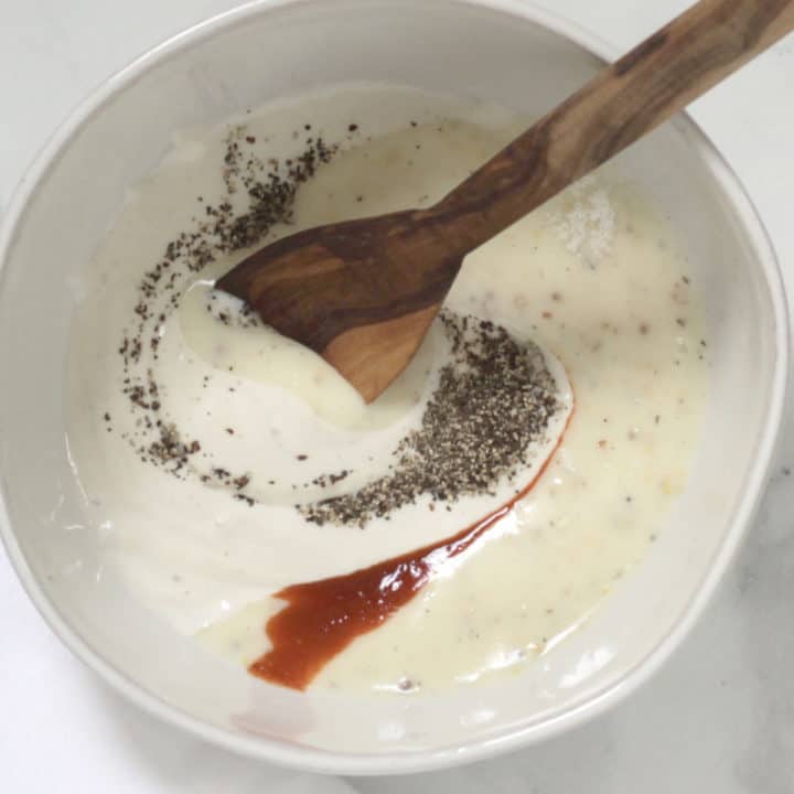 ground black pepper and red hot sauce are stirred in swirls into creamy white sauce