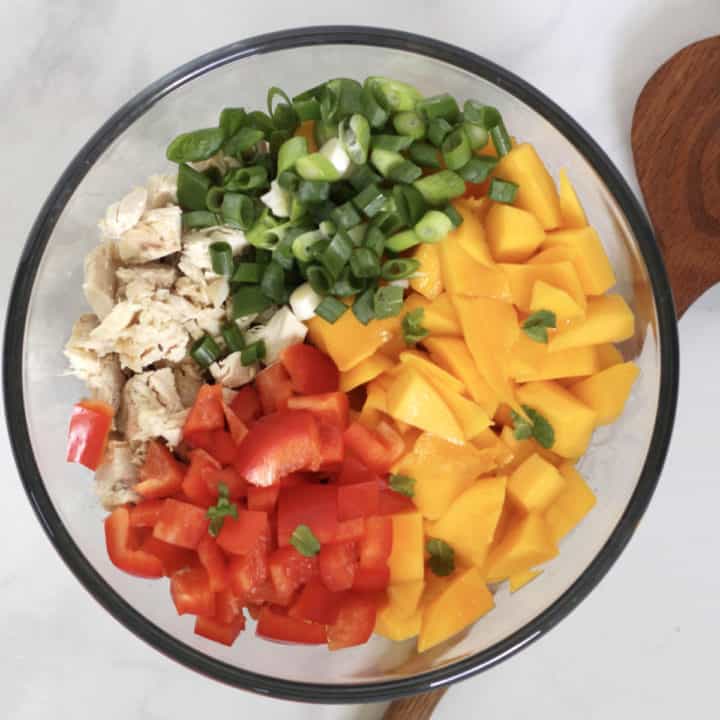 looking down on glass bowl of chunks of mango, red pepper, cooked chicken, and green onion