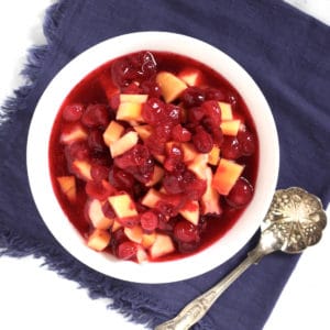 looking down on cranberry sauce with chunks of mango in a white bowl on a lavendar napkin