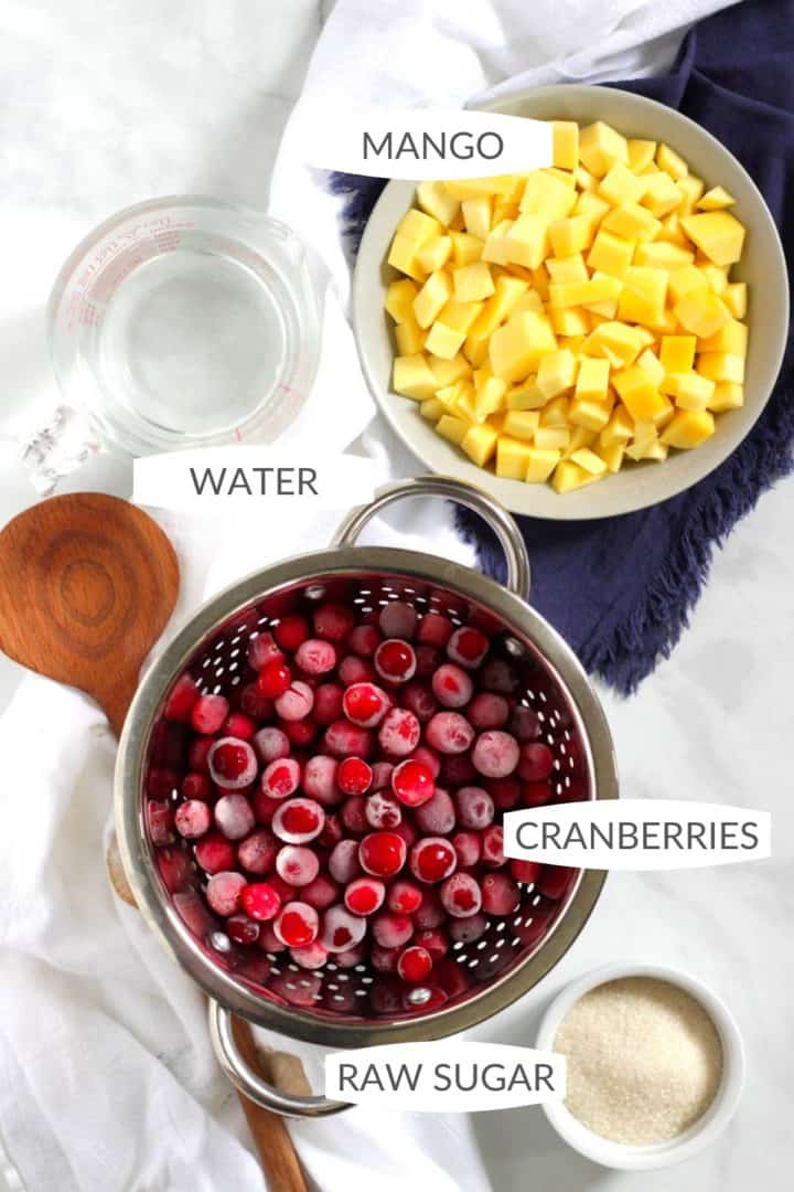looking down on bowls of frozen cranberries, chopped mango, raw sugar, and water, with labels