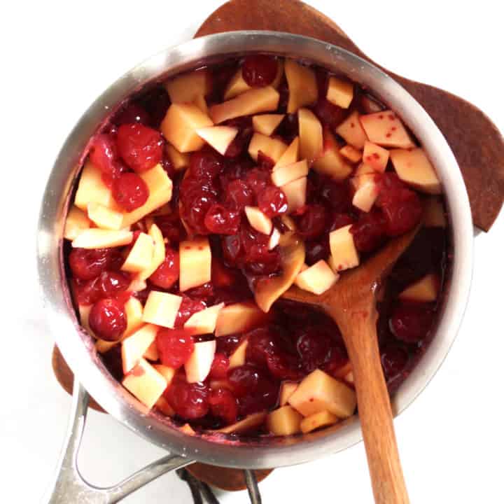 chunks of mango being stirred into cranberry sauce in saucepan